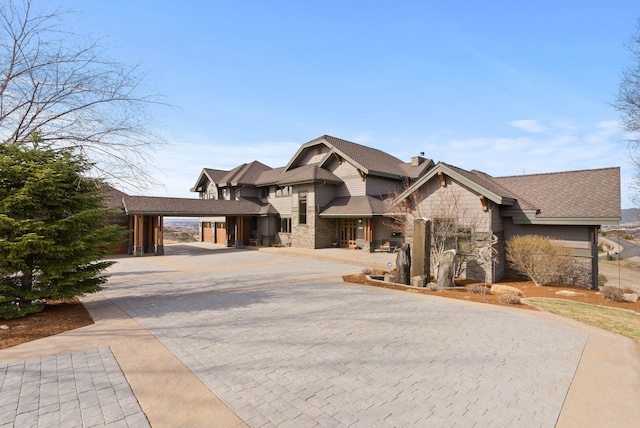 view of front of house featuring stone siding, a chimney, and decorative driveway