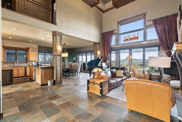 living area with recessed lighting, stone finish flooring, a towering ceiling, and ornate columns