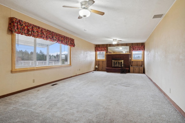 unfurnished living room with visible vents, carpet, baseboards, a brick fireplace, and ceiling fan