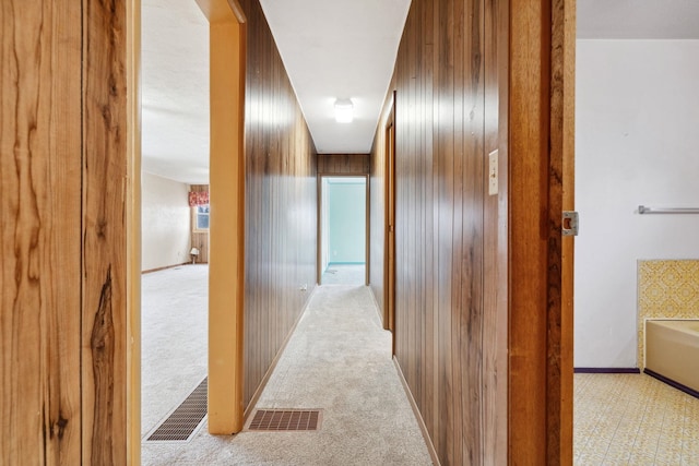 hallway featuring visible vents, baseboards, light colored carpet, and wood walls