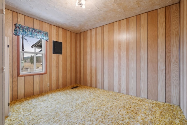 spare room with electric panel, carpet flooring, wood walls, and visible vents