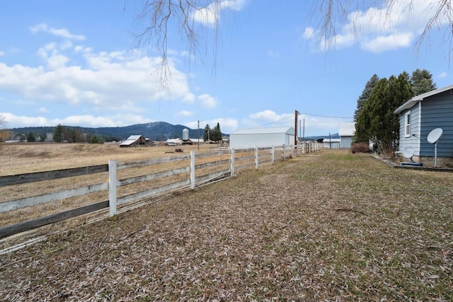 view of yard with a rural view, fence, and a mountain view