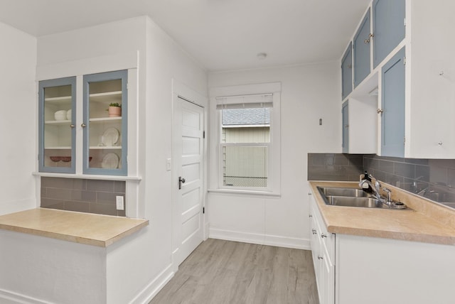 kitchen featuring a sink, blue cabinetry, backsplash, light wood-style floors, and light countertops