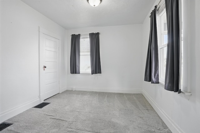 spare room featuring carpet flooring, visible vents, a textured ceiling, and baseboards