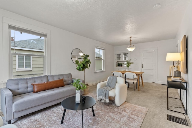 living room with visible vents, baseboards, light colored carpet, and a textured ceiling