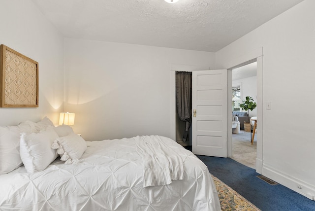 bedroom with visible vents, a textured ceiling, baseboards, and dark colored carpet