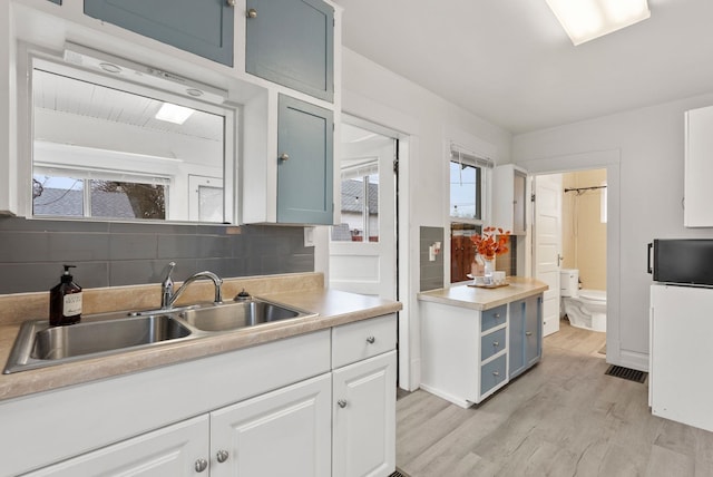 kitchen featuring a sink, decorative backsplash, light countertops, white cabinetry, and light wood-type flooring