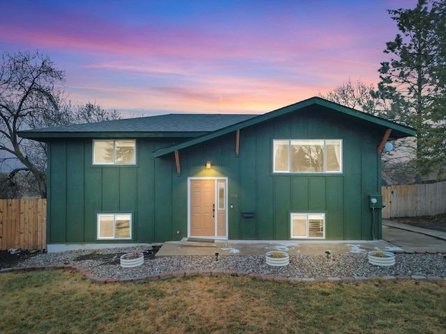 view of front facade featuring board and batten siding, a shingled roof, a front lawn, and fence