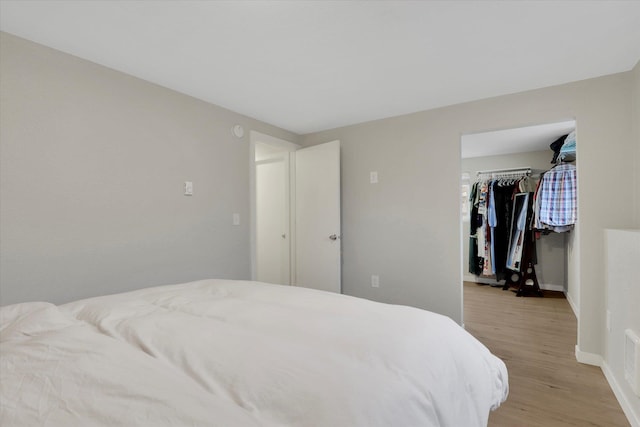 bedroom featuring a spacious closet, a closet, baseboards, and light wood-style floors