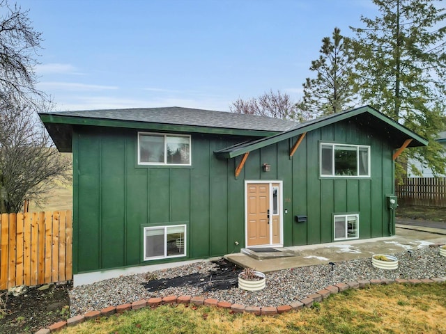 bi-level home featuring a patio area, fence, board and batten siding, and a shingled roof