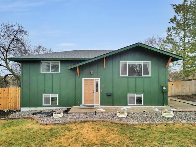 bi-level home featuring board and batten siding, a front yard, roof with shingles, and fence