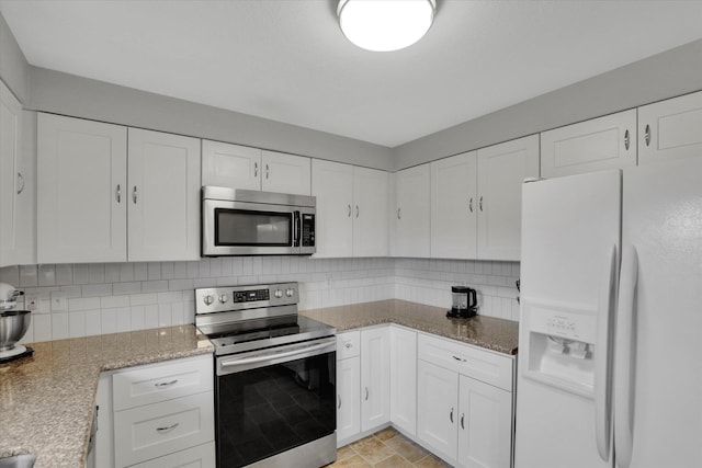 kitchen featuring stone finish flooring, white cabinetry, stainless steel appliances, decorative backsplash, and light stone countertops