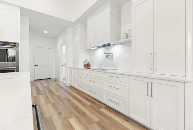 kitchen featuring white cabinetry, double oven, light wood-style flooring, and wall chimney exhaust hood