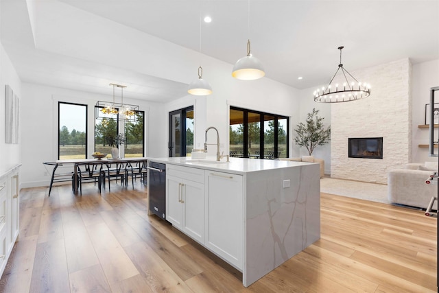 kitchen featuring a sink, light wood-style flooring, a stone fireplace, and a chandelier