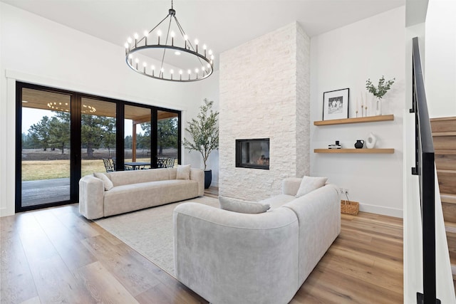 living room featuring a stone fireplace, an inviting chandelier, wood finished floors, and baseboards