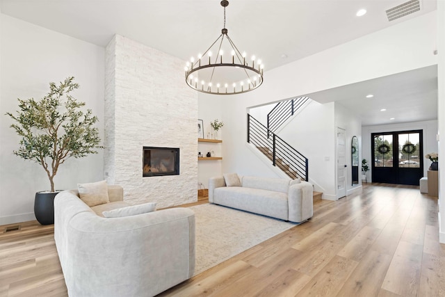 living room with visible vents, a notable chandelier, stairway, a stone fireplace, and light wood finished floors