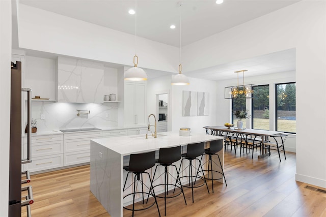 kitchen with visible vents, light wood-style flooring, a sink, backsplash, and black electric cooktop