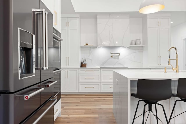 kitchen with light wood-type flooring, a kitchen bar, tasteful backsplash, white cabinetry, and high end refrigerator