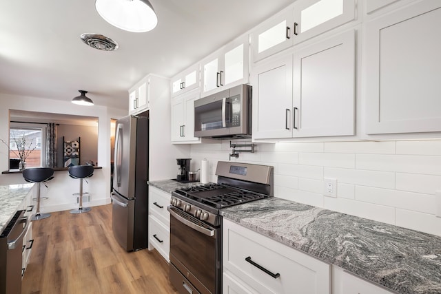 kitchen with visible vents, backsplash, glass insert cabinets, stainless steel appliances, and white cabinetry