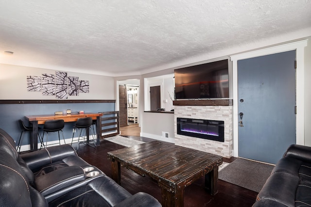 living room with a glass covered fireplace, a textured ceiling, visible vents, and wood finished floors