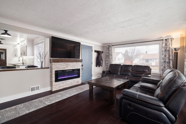 living area with visible vents, dark wood-type flooring, a textured ceiling, a fireplace, and baseboards