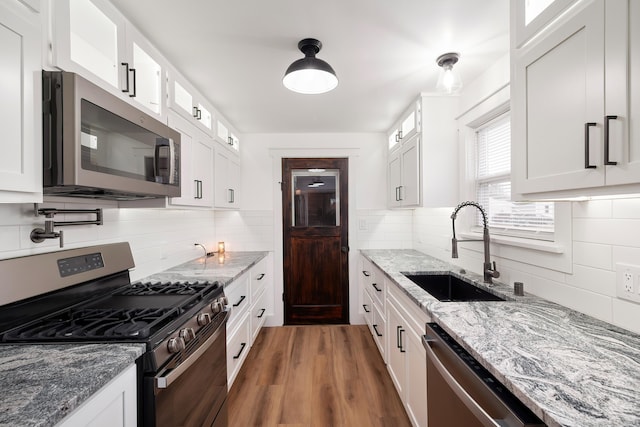 kitchen with a sink, white cabinets, tasteful backsplash, and stainless steel appliances