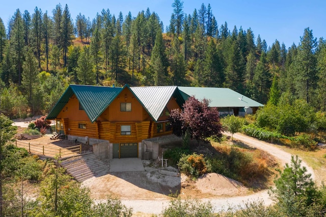 view of front of home featuring a forest view, driveway, an attached garage, log exterior, and metal roof