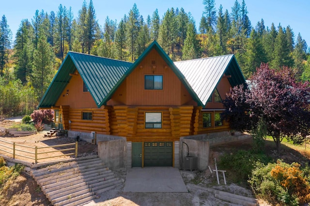 cabin featuring concrete driveway, log exterior, an attached garage, and metal roof