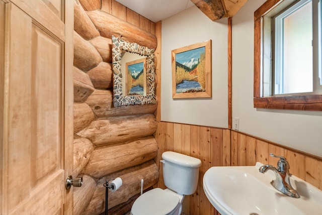 half bathroom featuring rustic walls, wainscoting, toilet, and a sink