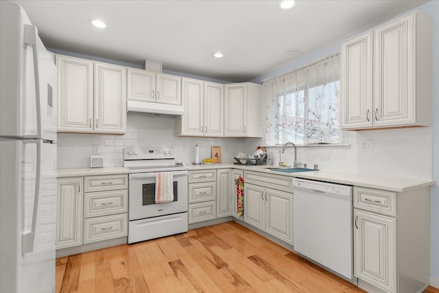 kitchen featuring light wood-type flooring, a sink, under cabinet range hood, white appliances, and light countertops