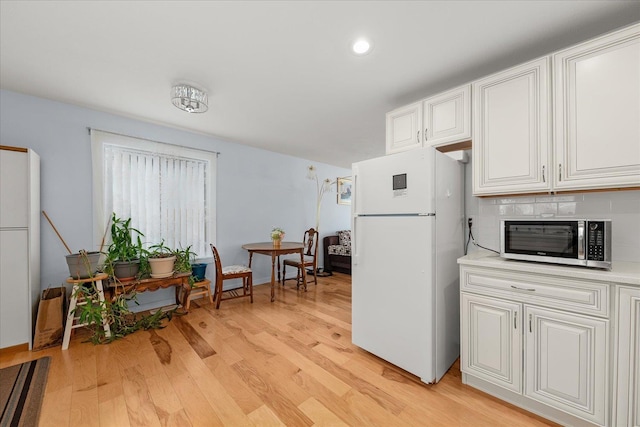 kitchen featuring stainless steel microwave, light wood-style floors, freestanding refrigerator, and light countertops