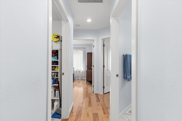 hall with light wood finished floors, visible vents, baseboards, and a textured wall