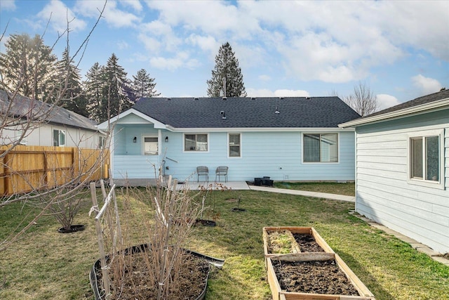 rear view of house featuring a lawn, a patio, fence, a shingled roof, and a garden