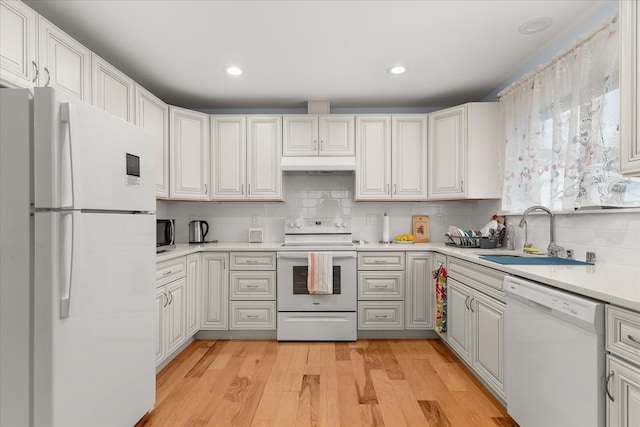 kitchen with white appliances, light wood finished floors, a sink, light countertops, and under cabinet range hood