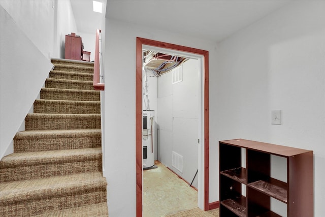 stairway featuring visible vents, carpet floors, and electric water heater