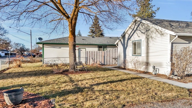 rear view of house with a yard, fence, and roof with shingles