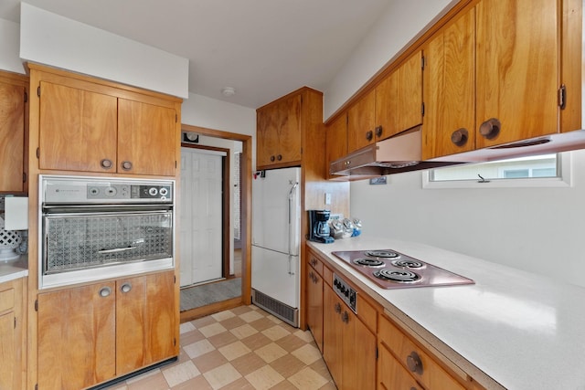 kitchen with brown cabinets, under cabinet range hood, stainless steel appliances, light countertops, and light floors