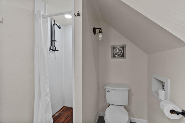 bathroom with baseboards, toilet, vaulted ceiling, a shower with curtain, and wood finished floors