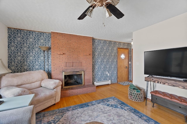 living room featuring a brick fireplace, ceiling fan, wood finished floors, a textured ceiling, and a baseboard radiator