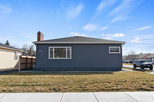 view of home's exterior featuring a lawn, a chimney, and fence