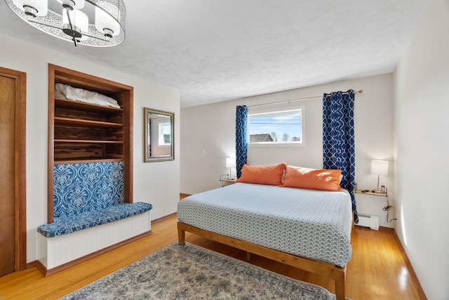 bedroom featuring a chandelier, baseboard heating, baseboards, and light wood-style floors