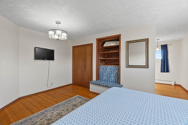 bedroom with a baseboard heating unit, an inviting chandelier, wood finished floors, and two closets