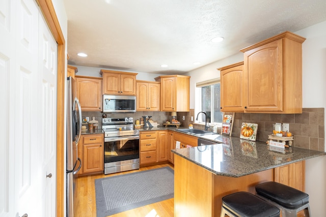 kitchen featuring a peninsula, a sink, light wood-style floors, appliances with stainless steel finishes, and tasteful backsplash