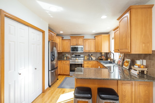 kitchen featuring light wood finished floors, a peninsula, a sink, appliances with stainless steel finishes, and a kitchen breakfast bar