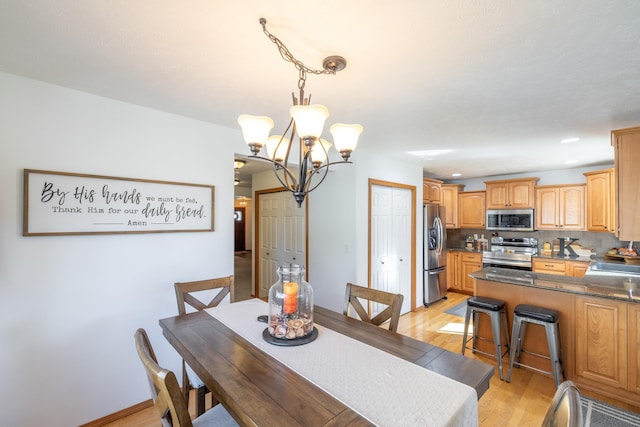 dining room featuring light wood-type flooring, baseboards, and a notable chandelier