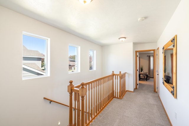 corridor featuring an upstairs landing, light colored carpet, and baseboards