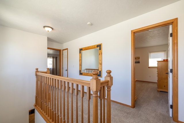 hallway featuring carpet flooring, an upstairs landing, baseboards, and a textured ceiling