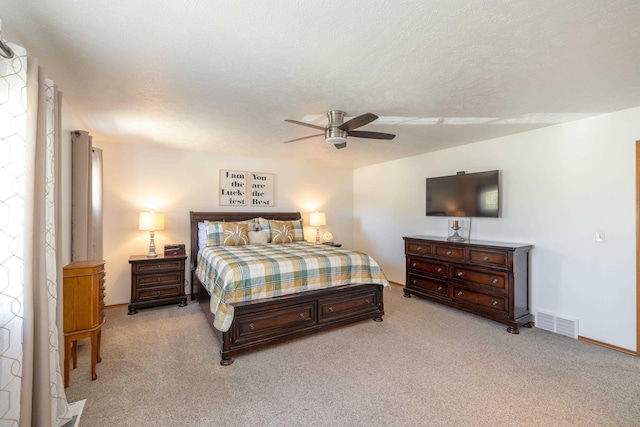 bedroom featuring visible vents, light colored carpet, a textured ceiling, and ceiling fan