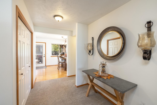 corridor featuring a textured ceiling, baseboards, and light carpet