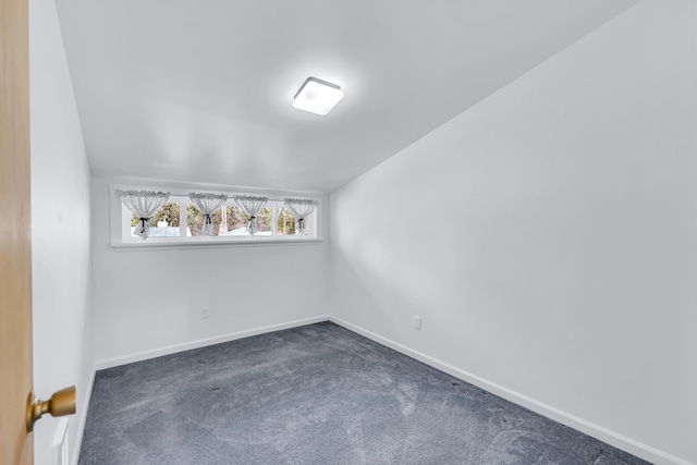 empty room with dark carpet, lofted ceiling, and baseboards